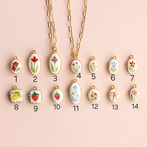 Detailed grid of fourteen floral and fruit enamel pendants with various artistic patterns