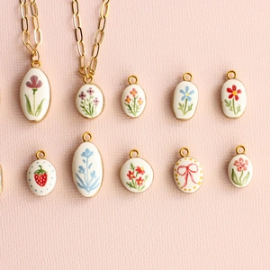 Detailed view of handmade ceramic pendants with floral and strawberry motifs on pink background