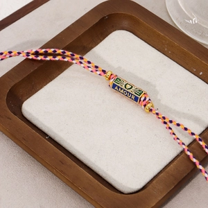 Detail of hand-woven multicolor cord bracelet with gold AMOUR engraved metal charm