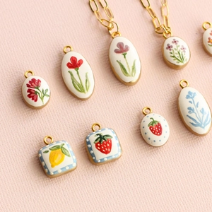 Macro shot of assorted hand-painted floral, strawberry, and lemon pendants with gold plating
