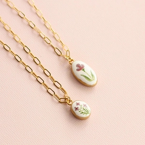 Detail of gold paperclip chain necklace with floral ceramic oval pendants on pink background