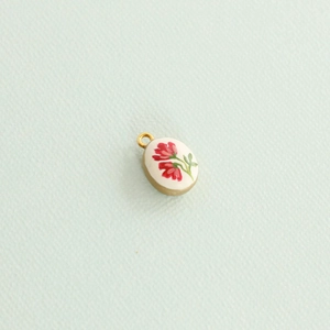 Close-up of golden oval pendant featuring delicate red floral painting and white base
