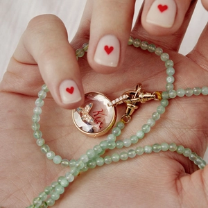 Détail d'un médaillon doré avec papillon et texte sur un collier de perles vertes