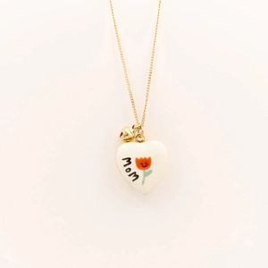 Détail du médaillon cœur plaqué or 18k avec texte MOM et pendentif fleur orange souriant