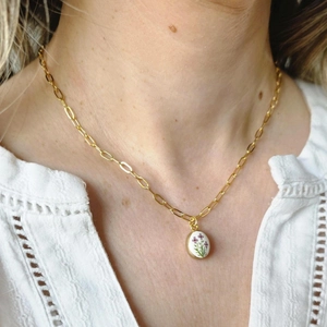 Gold paperclip necklace with oval floral pendant worn on a white lace blouse