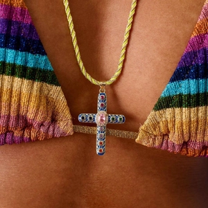 Détail d'un pendentif croix coloré avec émail et cordon tressé sur la plage d'été