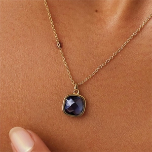 Detalle macro de un colgante cuadrado con piedra azul oscuro en un collar dorado fino