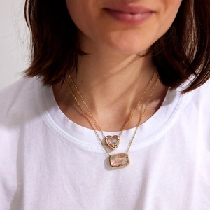 Détail de colliers dorés superposés avec pendentifs médaillons cœur et rectangle MISS