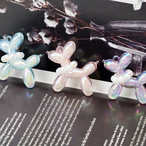 Three colorful pearlescent resin balloon dog charms with pearl collars on a magazine