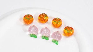 Detail of transparent glass persimmon and peach pendants on a white display tray