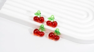 Macro detail of four translucent cherry-shaped glass charms with green leaf stems on a stand