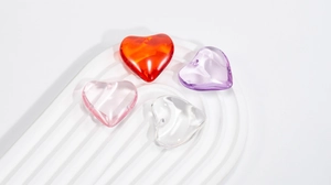 Close-up of four colorful heart-shaped acrylic resin beads with hole for DIY jewelry