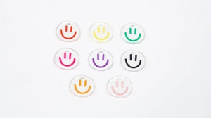 Flat lay of eight colorful transparent acrylic smiley face charms for DIY jewelry making