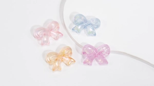 Close-up of glittery acrylic bow beads in pastel pink blue and purple for DIY jewelry