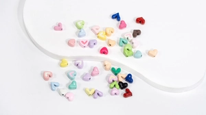 Bunte herzförmige Perlen für DIY-Schmuck auf weißem Display-Board verteilt