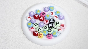 Makroaufnahme bunter Acryl-Alphabetperlen in einer weißen Schale für DIY-Schmuckbau