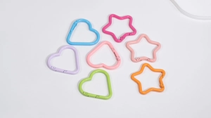 Dettaglio di ganci a scatto colorati in lega a forma di cuore e stella per borse