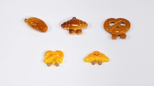 Close-up of cute resin bread pendants including croissant and pretzel with cartoon faces