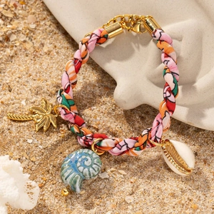 Détail d'un bracelet de plage tissé avec des breloques tropicales posé sur du sable