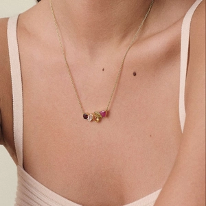 Detail of gold necklace featuring a cluster of five colorful gems on a delicate cross chain