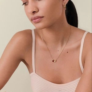 Detail of gold necklace with rectangular ruby and opal pendants worn by a model