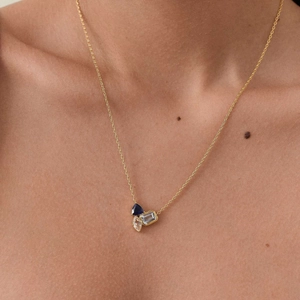 Detail of elegant gold necklace featuring red and blue crystal pendant on woman's neck
