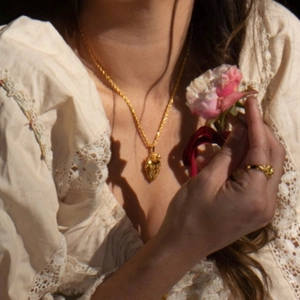 Collana vintage dorata con ciondolo fragola 3D indossata su una camicia di pizzo
