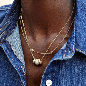 Gros plan d'un collier double épaisseur doré avec trèfle et breloques pavées sur modèle