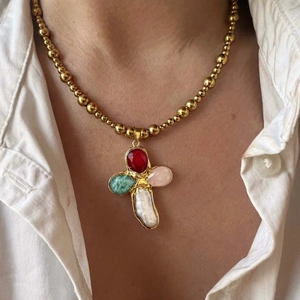 Close-up of titanium cross necklace with colorful gemstones and baroque pearl on white shirt