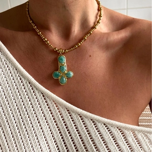 Close-up of a bohemian gold bead necklace with a green natural stone cross flower pendant