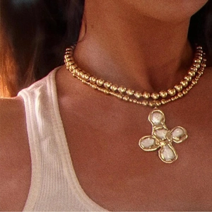 Close-up of double-layered gold bead chain necklace with white floral cross pendant