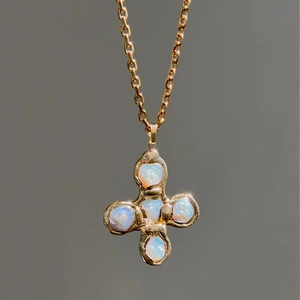 Detail of golden pebble texture cross necklace featuring iridescent white gemstones