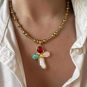 Macro detail of gold beaded necklace with colorful gemstone and pearl cross pendant