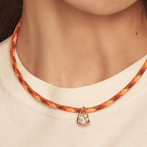 Macro detail of a colorful woven rope necklace featuring a sparkling triangle zircon pendant