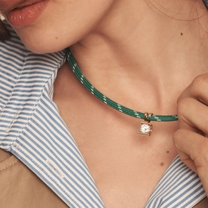 Close-up of a green braided rope necklace with a square gold pendant and round zircon stone