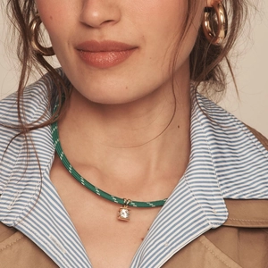 Close-up of woven green cord necklace with square zircon pendant and gold hoop earrings