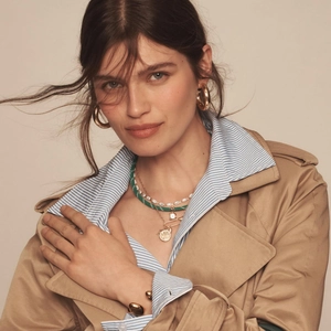 Detail of layered jewelry featuring green braided rope, pearls, and gold zircon necklace