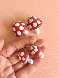 Detailed view of handmade red and white mushroom earrings with golden hoops on hand