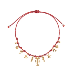 Macro detail of ocean-themed necklace with gold fishbone and seahorse charms on braided rope