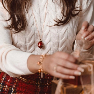 Pendentif en forme d'œuf rouge avec chaîne en or rose sur pull en maille blanc