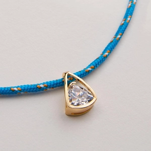 Macro shot of a geometric triangle gold pendant with zircon and colorful braided rope cord