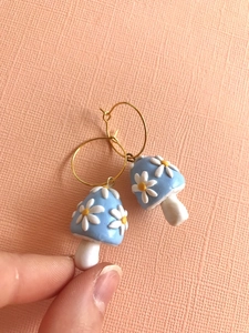 Detail of handmade blue mushroom earrings with white daisy patterns and gold hoops