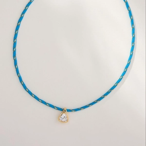 Detail of blue braided rope necklace with gold triangle pendant and clear zircon stone
