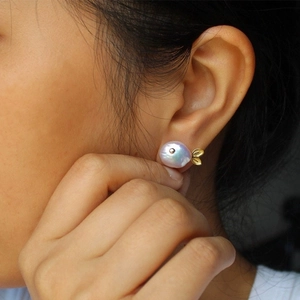 Close-up of a whale-shaped Baroque pearl earring with golden tail on model