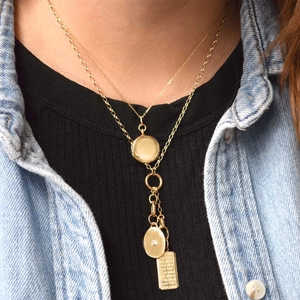 Close-up of layered gold necklace with engraved locket pendant and sparkling crystals