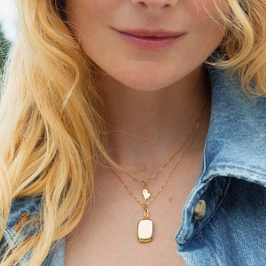 Close-up of a layered gold necklace set with heart and rectangle pendants on a model