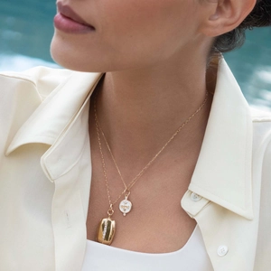 Detail of layered gold necklaces with white enamel bee pendant and zircon oval charm