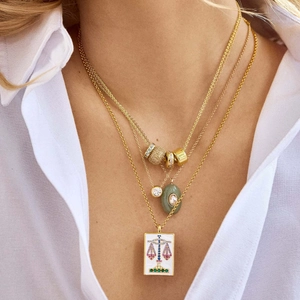 Detail of layered 18k gold plated necklaces with Libra pendant and green gemstone