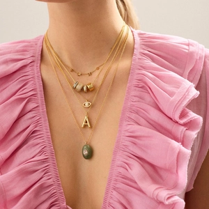 Macro shot of 18k gold layered necklaces featuring Evil Eye and green stone charms