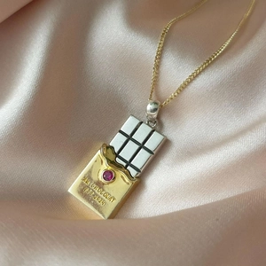 Macro detail of chocolate bar pendant with red gemstone on pink silk backdrop